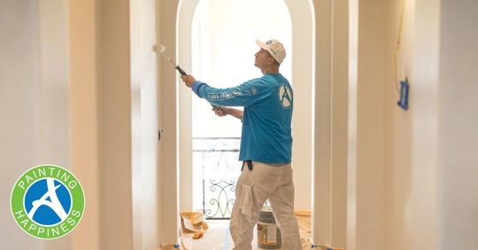 A man painting a hallway wall with a white roller